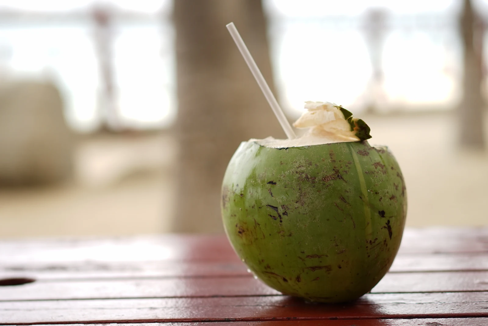 A fresh green coconut with a straw